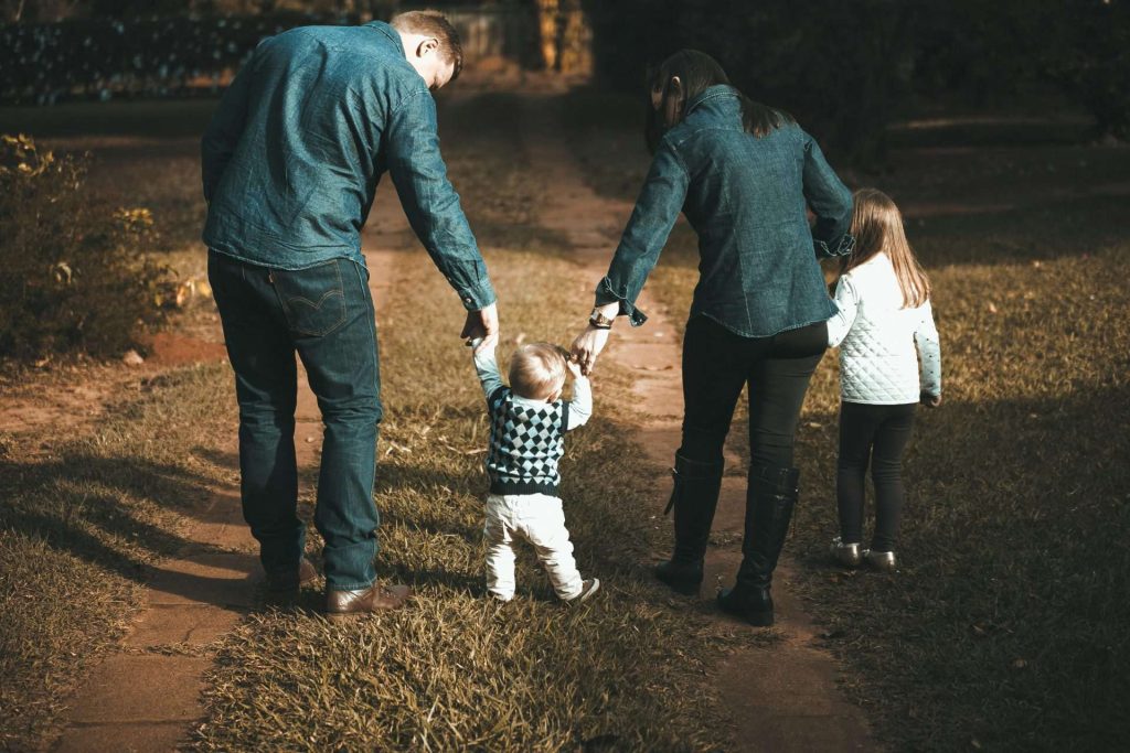 Une famille de quatre personnes marche main dans la main sur un sentier, profitant d'une journée ensoleillée en plein air.