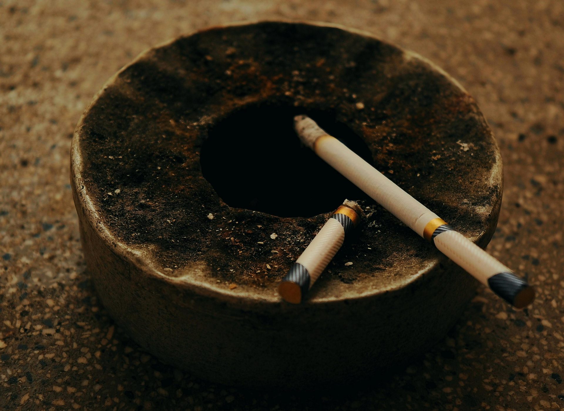 Un cendrier antique avec deux cigarettes brûlées sur une surface texturée, créant une atmosphère maussade.