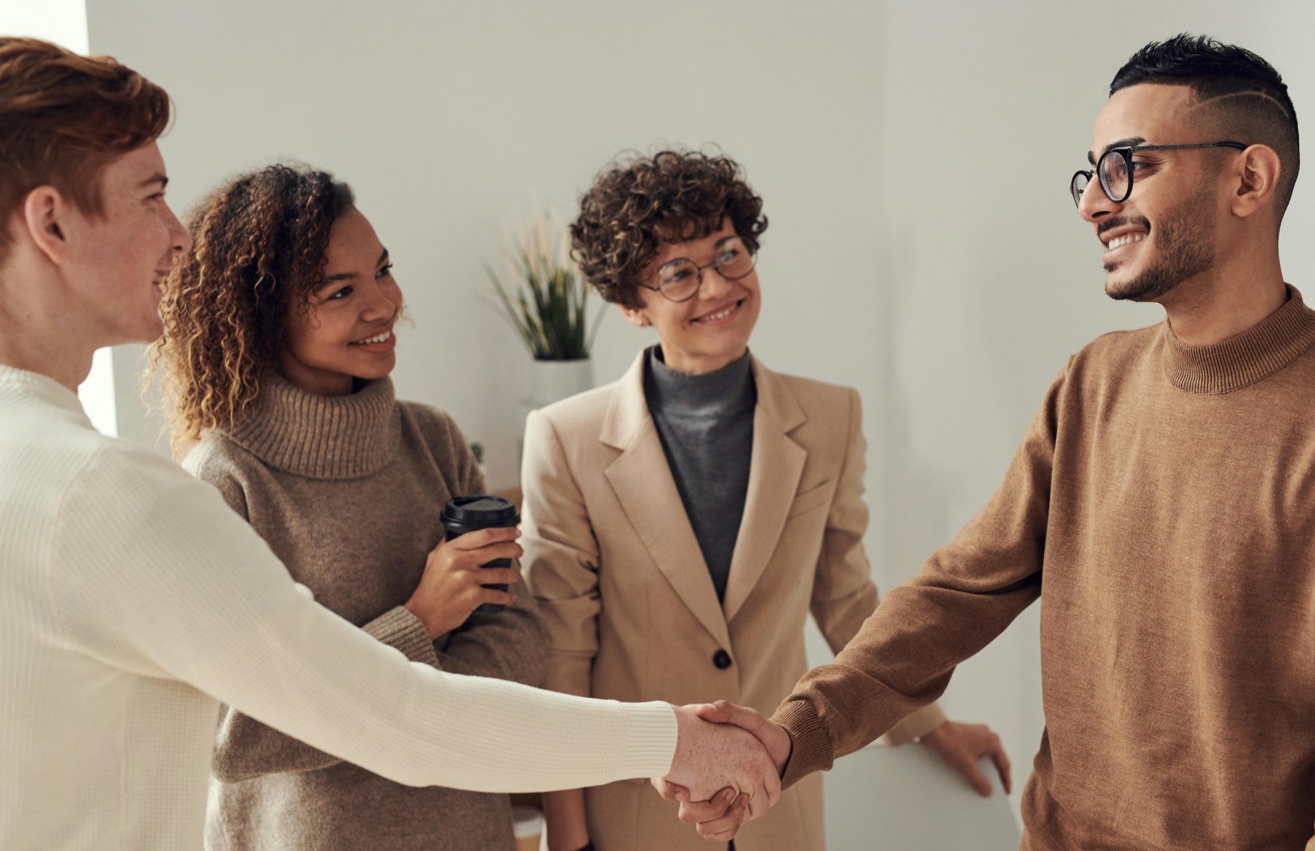 Groupe diversifié de jeunes adultes se serrant la main dans un environnement de bureau, illustrant le travail d'équipe et la collaboration.
