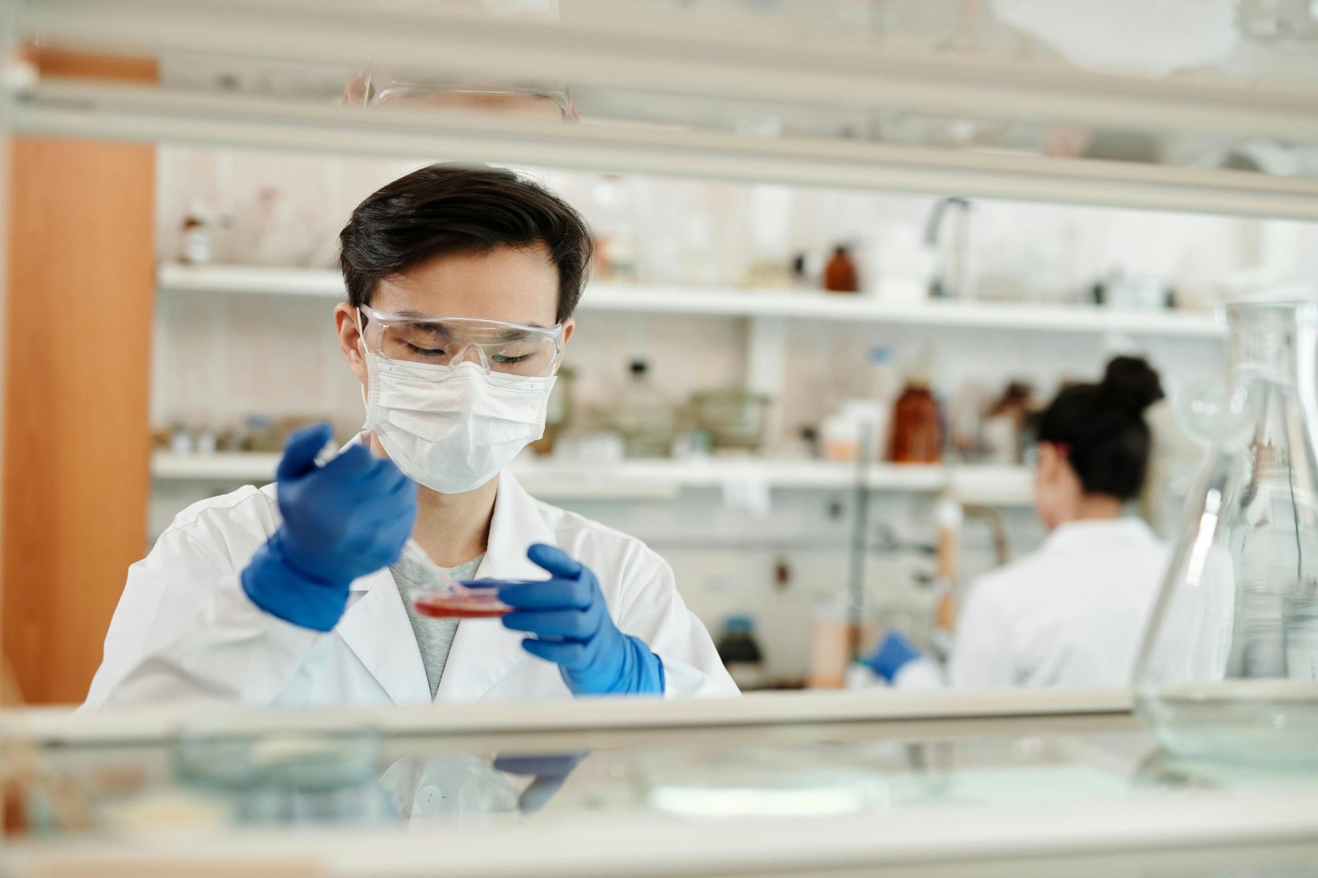 Chercheur en blouse de laboratoire travaillant sur une expérience scientifique avec une boîte de Pétri et un équipement de protection.