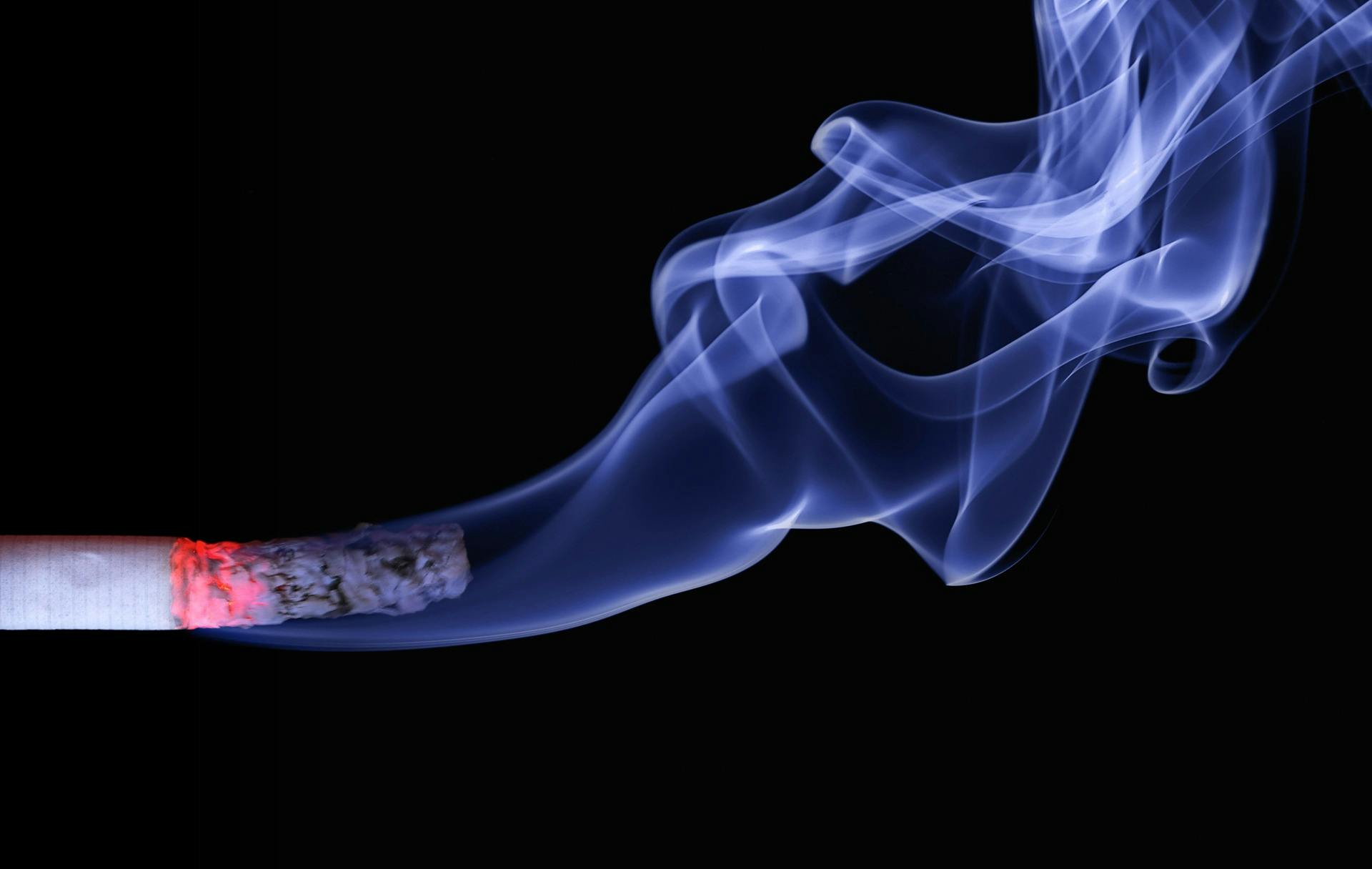 Gros plan détaillé d'une cigarette avec des braises incandescentes et de la fumée tourbillonnante sur un fond noir.