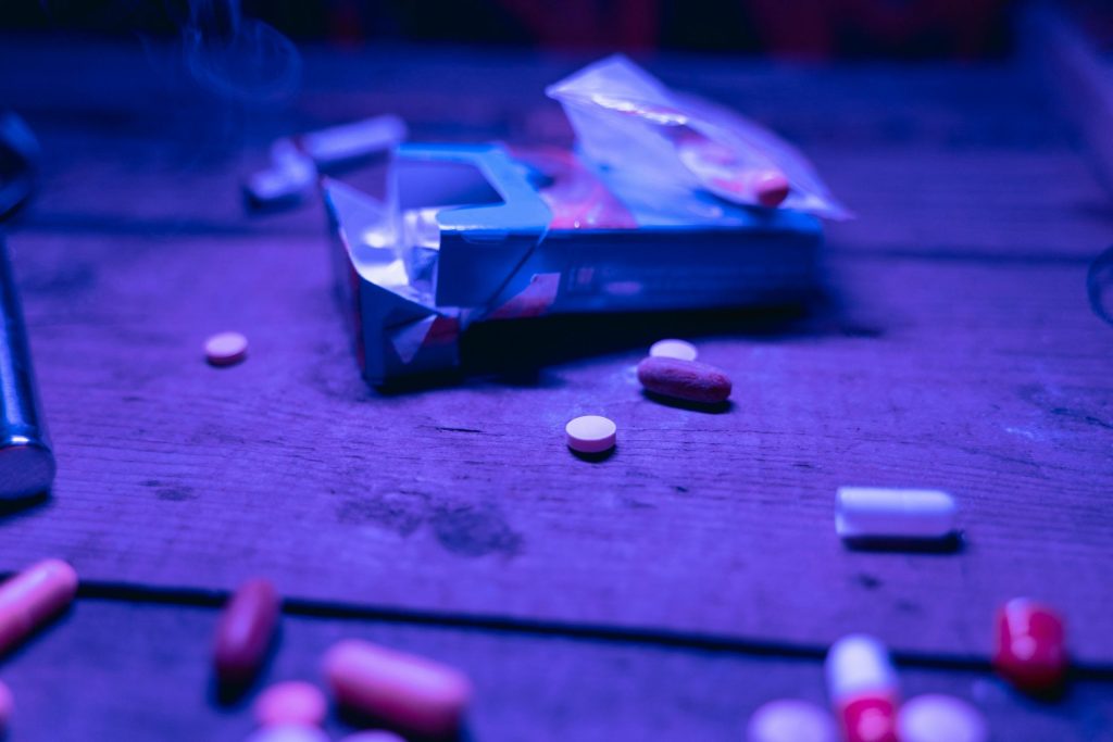 Diverses pilules dispersées sur une table en bois sous une lumière violette, représentant un concept de médicament ou de substance.