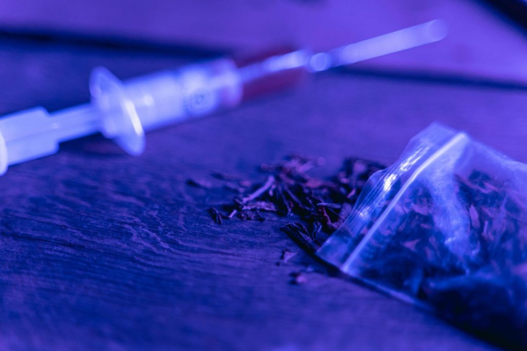 Gros plan d'une seringue et d'un sac de substance séchée avec un éclairage bleu.